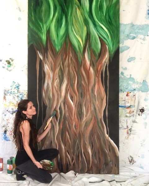 Michelle Pier Artist kneeling beside a painting of a Guam Tree